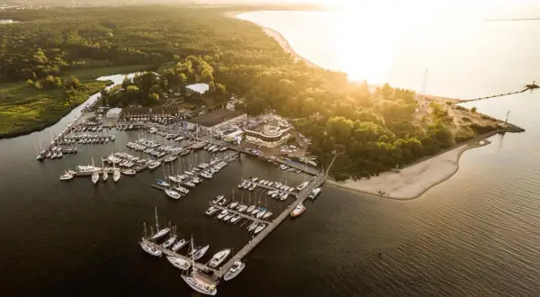 Zachód słońca nad zatoką, gdzie cumują liczne jachty. Widok na górki zachodnie marina, otoczoną zielenią i piaszczystą plażą.