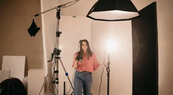 Kobieta z aparatem w studiu fotograficznym, otoczona sprzętem. Pokazuje, jak ustawić lampę błyskową w aparacie, by uzyskać idealne światło.