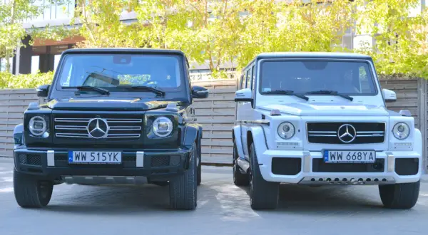 Dwa luksusowe Mercedesy klasy G, czyli gelendy, stoją obok siebie. Jedna jest ciemnozielona, druga biała.