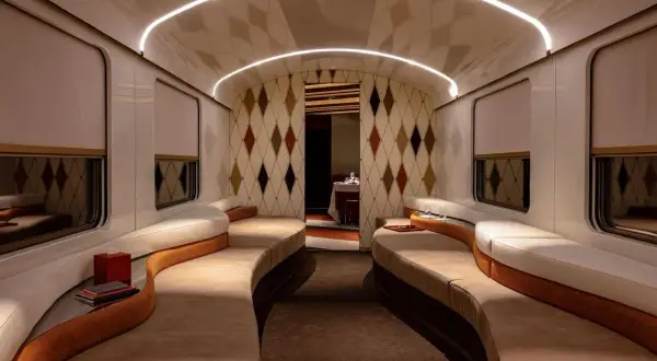 Luxuriöses Interieur eines Nachtzugs nach Italien mit geschwungenen Sofas, Rautenmuster-Tapete und indirekter Beleuchtung.