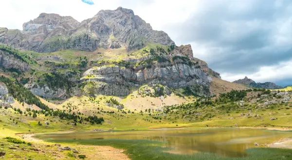 El ibón Piedrafita, un espejo de agua sereno, refleja la majestuosidad de las montañas rocosas y verdes.