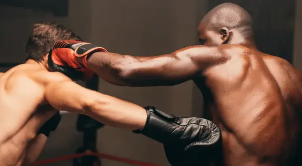 Two boxers in a ring, one landing a powerful cross combination punch. Sweat glistens on their muscular bodies.