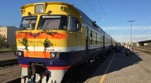 Gelber Zug mit grüner Deko am Bahnhof, bereit für die Fahrt von Riga nach Tallinn.