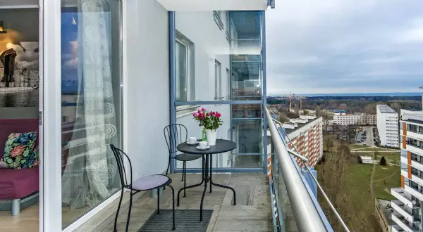 Balkon z widokiem na Gdańsk Przymorze. Stolik z kawą i kwiatami czeka na gości.