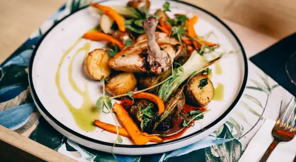 Pyszne danie z kurczaka z ziemniaczkami i marchewką, ozdobione ziołami. Idealna pozycja z **Fischgarten menu**.