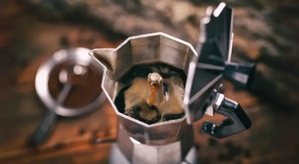 Caffettiera moka in primo piano, con il caffè che sale. Un rituale mattutino che, si dice, il caffè aiuta a digerire.