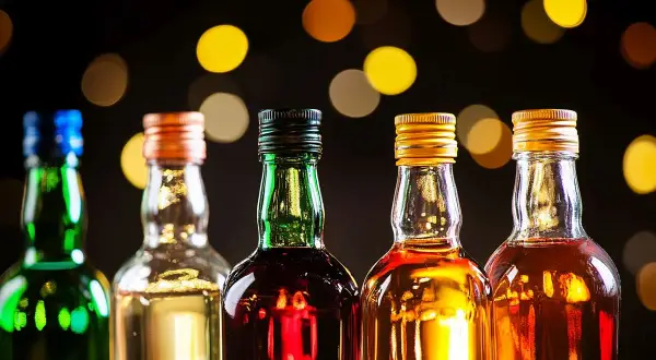 Rząd pięciu butelek z różnymi alkoholami, w tym zielona z niebieskim korkiem, przezroczysta z pomarańczowym, zielona z czarnym, przezroczysta ze złotym i przezroczysta z kolejnym złotym. Tło rozmyte, z ciepłymi, okrągłymi światłami. Idealne na wieczór ...