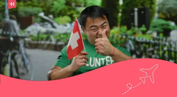 Hombre con bandera suiza y camiseta de voluntario, pulgar arriba. ¡Orgulloso de su voluntariado suizo!