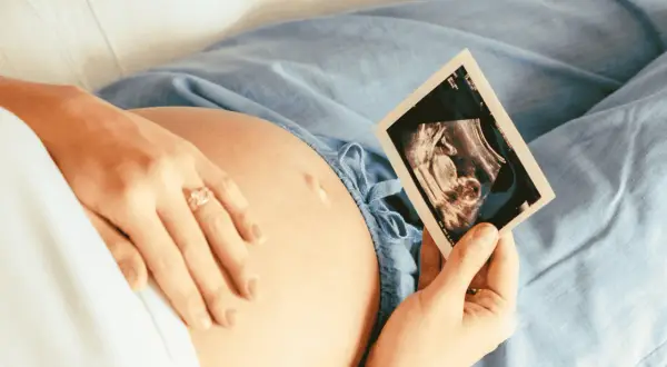 Kobieta trzyma kartę ciąży, patrząc na zdjęcie USG swojego dziecka.