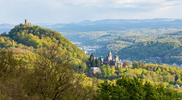 Majestätische Burg Drachenfels thront über einem grünen Tal mit einem Fluss und weiteren Burgen.