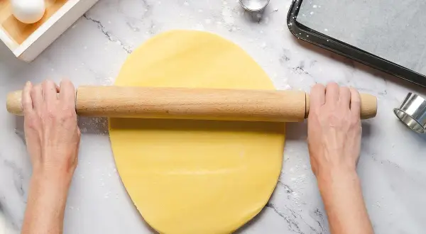 Mani stendono la pasta frolla senza burro con un mattarello. Ingredienti per dolci leggeri.