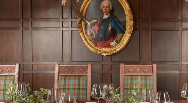 Un ritratto regale domina la sala da pranzo, con sedie a quadri e un tavolo apparecchiato, un'ambientazione che evoca i migliori ristoranti di Londra.