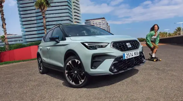 Jasnoszary SEAT Arona, jeden z najnowszych seat modele, zaparkowany obok młodej kobiety na deskorolce.
