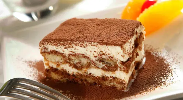 En bit krämig italiensk dessert, tiramisu, pudrad med kakao. Garnerad med apelsin och körsbär.
