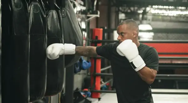 Man in white boxing gloves throws a punch at a heavy bag, demonstrating how to practice boxing without a bag.