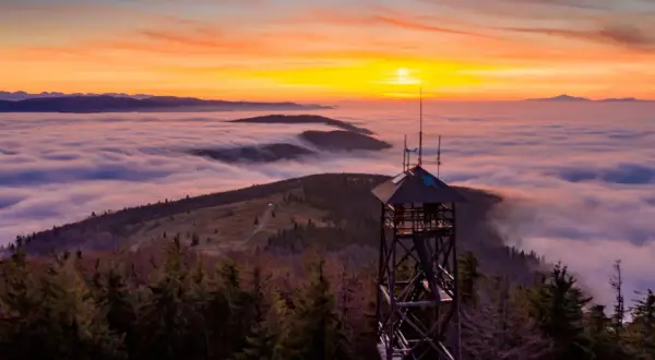 Wieża widokowa na Mogielicy góruje nad morzem chmur podczas zachodu słońca.