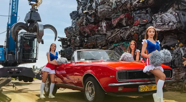 Trzy cheerleaderki z pomponami pozują przy czerwonym kabrioletcie na tle sterty złomu. To może być ciekawy widok dla kogoś szukającego auto szrot bydgoszcz.
