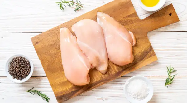 Tre petti di pollo crudi su tagliere, con pepe nero, sale, rosmarino e olio. Ideale per un pasto leggero, con poche calorie petto di pollo.