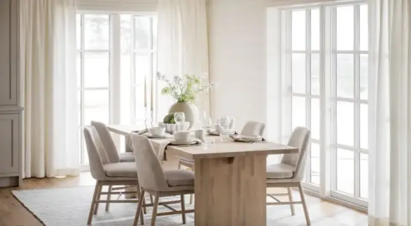 Ljus och luftig matplats med inspiration från naturen. Träbord, beiga stolar och stora fönster med vita gardiner skapar en harmonisk känsla.