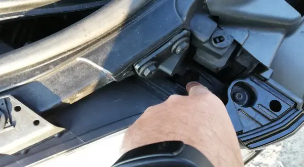 Palec wskazuje śrubę mocującą reflektor podczas wymiany żarówki audi a4 b7 przód prawa.