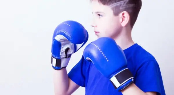 Young boxer in a wide boxing stance, wearing blue gloves and shirt, ready to fight.