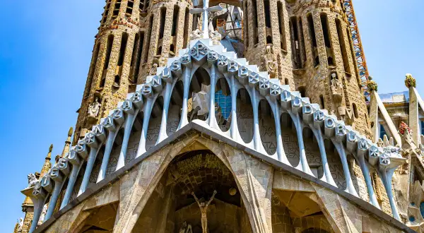 Intricate Gaudi art adorns the Sagrada Familia, with stone carvings and arched facades reaching towards a bright blue sky.