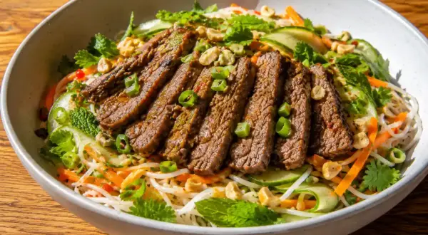 En skål med asiatisk biffsallad med nudlar, strimlad biff, gurka, morötter, mynta och jordnötter.