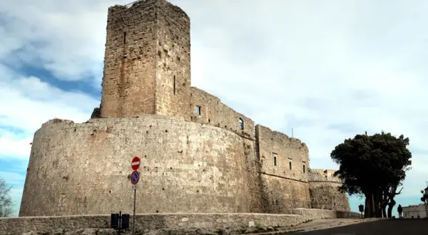 Imponente castello di Monte Sant'Angelo, con mura in pietra grezza e un torrione svettante sotto un cielo nuvoloso.