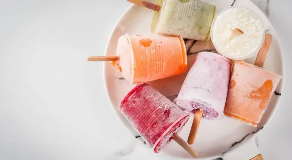Variopinti ghiaccioli fatti in casa su un piatto bianco: rossi, arancioni, rosa, verdi e bianchi al cocco.