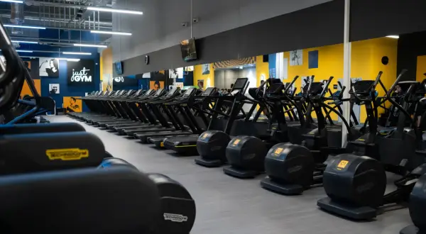 Rzędy bieżni i orbitreków w siłowni Just Gym. Chcesz wiedzieć, jak wejść na Multisport? Tu zaczynasz trening!