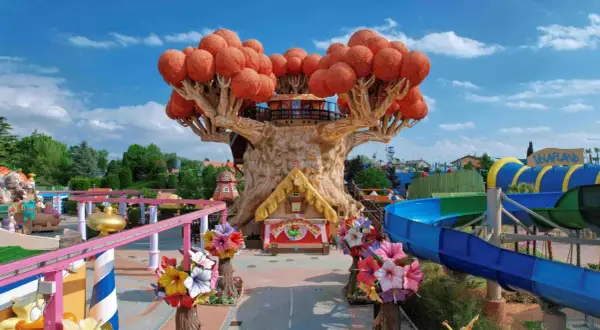 Un magico parco divertimenti in Italia con un albero gigante, scivoli acquatici e giostre colorate.