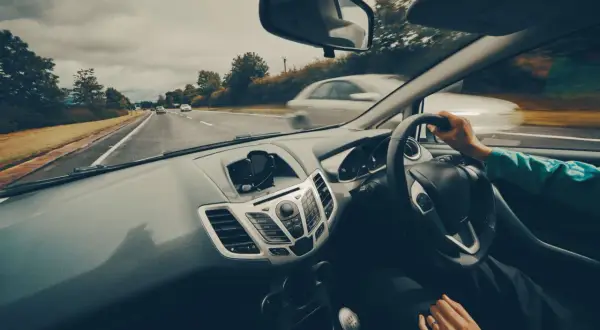 Widok z samochodu podczas jazdy po Polsce. Na desce rozdzielczej widoczny uchwyt na telefon. W tle droga i inne pojazdy. Dowód V5C rejestracja w Polsce.
