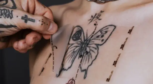 Frische tattoo pflege: Frischhaltefolie wird vorsichtig auf ein frisch gestochenes Schmetterlingstattoo auf der Brust aufgelegt.