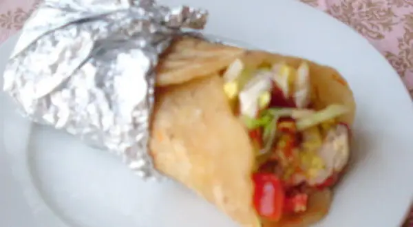 Pyszny kebab w cieście, zawinięty w folię aluminiową, z widocznymi warzywami i mięsem.