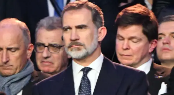 Król Hiszpanii Felipe VI w garniturze i krawacie, otoczony przez innych mężczyzn.