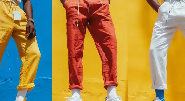 Tre män visar upp sina linnebyxor outfit herr i färgerna gult, orange och vitt mot en färgglad bakgrund.