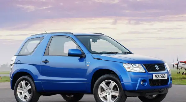 Niebieski Suzuki Grand Vitara 2005 na tle nieba z chmurami i samolotem.