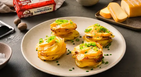 Gestapelte Kartoffeln mit geschmolzenem Käse und Schnittlauch. Daneben ein Block Limburger Käse, bereit für ein Romadur-Gericht.