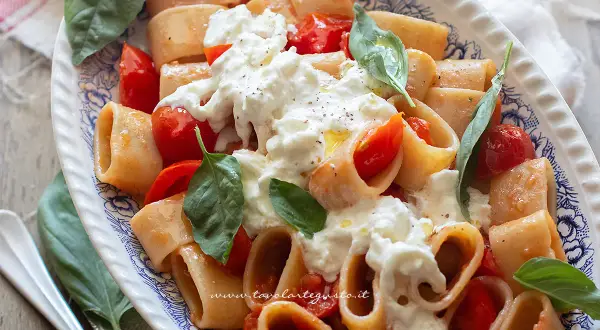 Piatto di pasta paccheri con pomodorini freschi e burrata cremosa, guarnito con basilico.