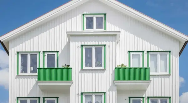 Vitt trähus med gröna detaljer runt fönster och balkonger. Ett perfekt hus att måla om för att fräscha upp.