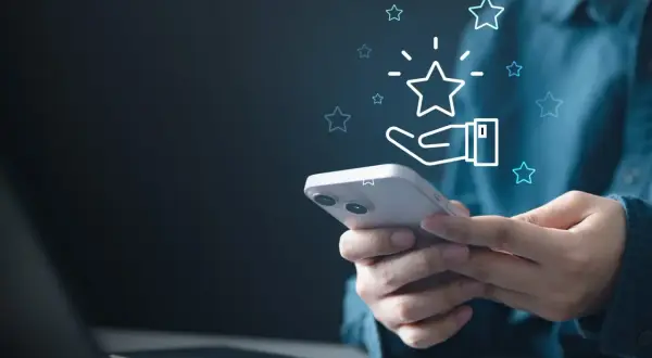 Dłoń trzymająca smartfon z ikoną gwiazdki i dłoni, symbolizującą ocenę.