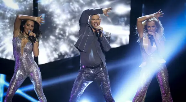 Yngves danskurser: Tre artister i glittriga scenkläder sjunger och dansar på en upplyst scen.