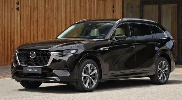 Elegancka, czarna Mazda CX-80 SUV stoi przed nowoczesnym budynkiem z drewnianą elewacją.
