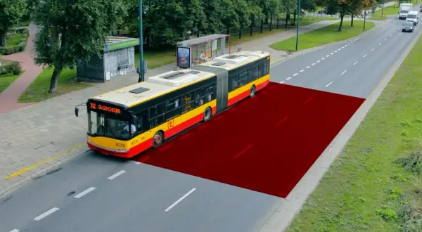 Czerwony obszar na drodze pokazuje bezpieczną odległość między samochodami w terenie zabudowanym, ilustrując przestrzeń dla autobusu.