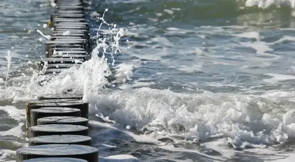 Fale rozbijają się o drewniane pale na plaży. Piękna, czerwcowa pogoda zachęca do spacerów brzegiem morza.