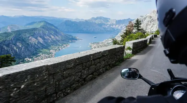 Widok z motocykla na Zatokę Kotorską w Czarnogórze. Kręta droga, kamienny mur i zapierająca dech w piersiach panorama gór i morza.