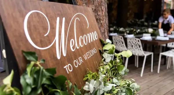 Drewniana tablica "Welcome to our wedding" z zielonymi liśćmi. Zastanawiasz się, kogo zaprosić na wesele?