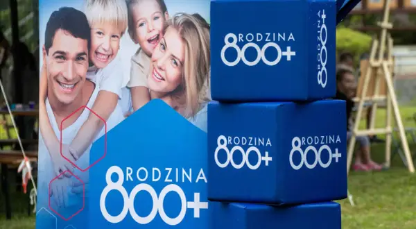 Uśmiechnięta rodzina na plakacie i niebieskie kostki z napisem "RODZINA 800+". Wniosek ZUS o świadczenie 800 plus to wsparcie dla rodzin.
