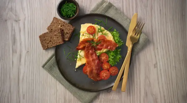 En härlig omelett i ugn med knaperstekt bacon, färska tomater, sallad och grovt bröd. Serveras med gräslök.