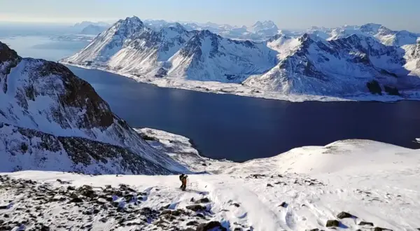 Ein Skifahrer genießt die atemberaubende Aussicht auf die schneebedeckten Berge und das tiefblaue Meer im **Lofoten Winter**.